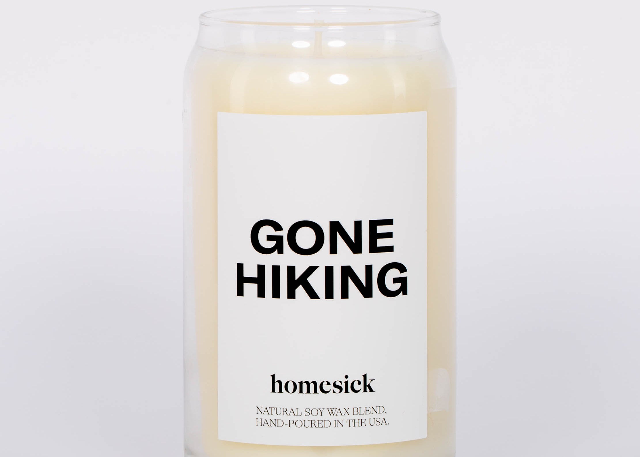 Gone Hiking Candle by Homesick. Glass jar with white candle and bold "GONE HIKING" label. White background.