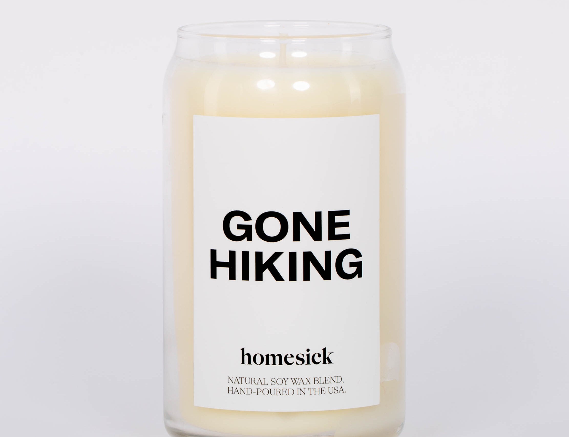 Gone Hiking Candle by Homesick. Glass jar with white candle and bold "GONE HIKING" label. White background.