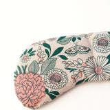 Migraine Mask by Slow North. Strap free cotton weighted eye pillow to be used hot or cold to sooth headaches and tired eyes. Tan and pink and green floral pattern. Zoom in on detail. White background.