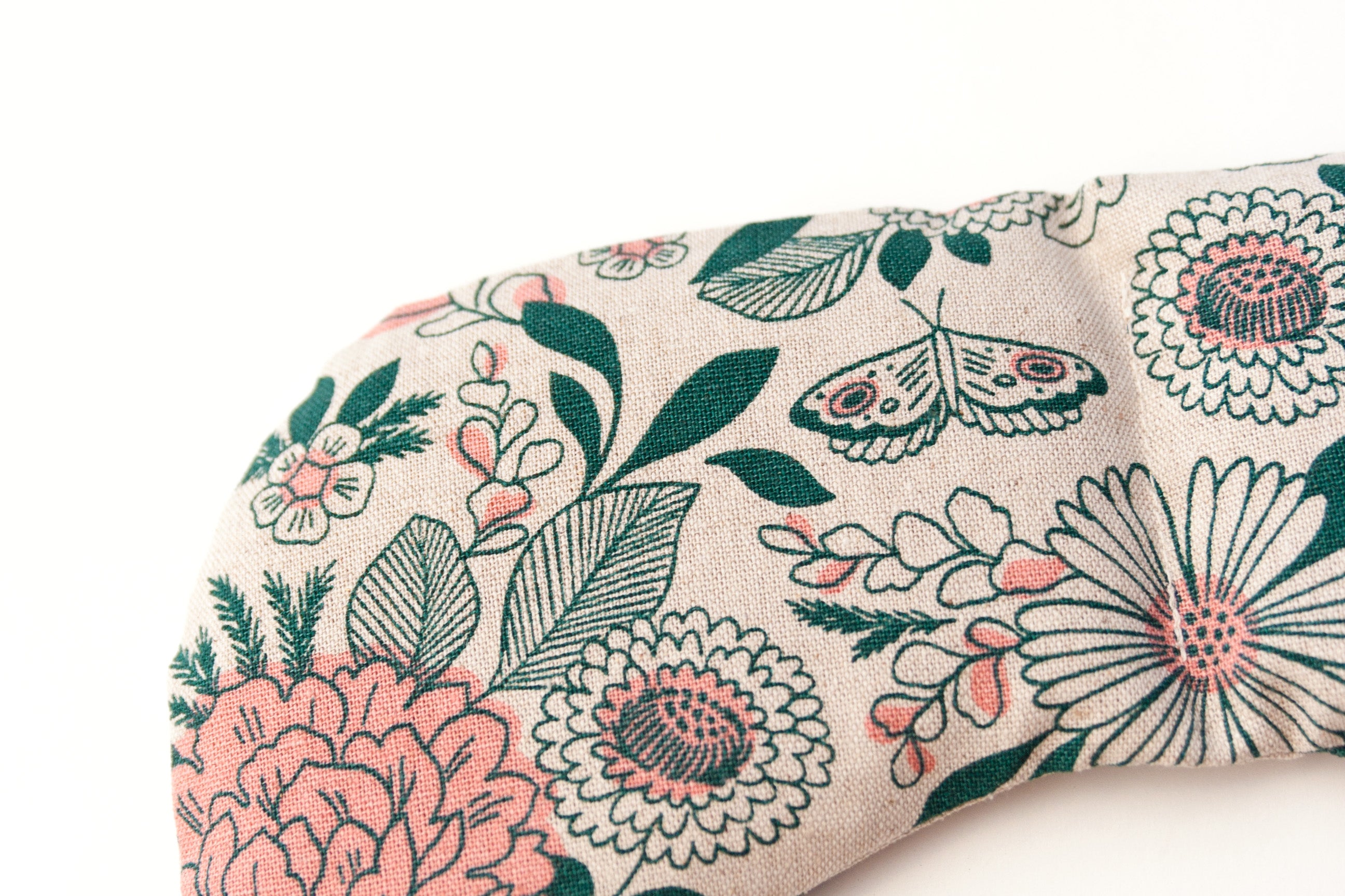 Migraine Mask by Slow North. Strap free cotton weighted eye pillow to be used hot or cold to sooth headaches and tired eyes. Tan and pink and green floral pattern. Zoom in on detail. White background.