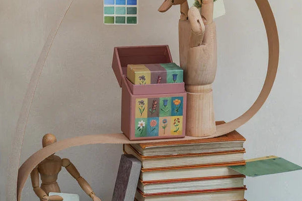 Wooden figures and books arranged on a circular shelf against a plain wall.