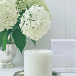 Fleur Blanche Cylindre white bubble glass candle by Alixx with moonflower and violet aroma. Hydrangeas bouquet and white interior setting. 