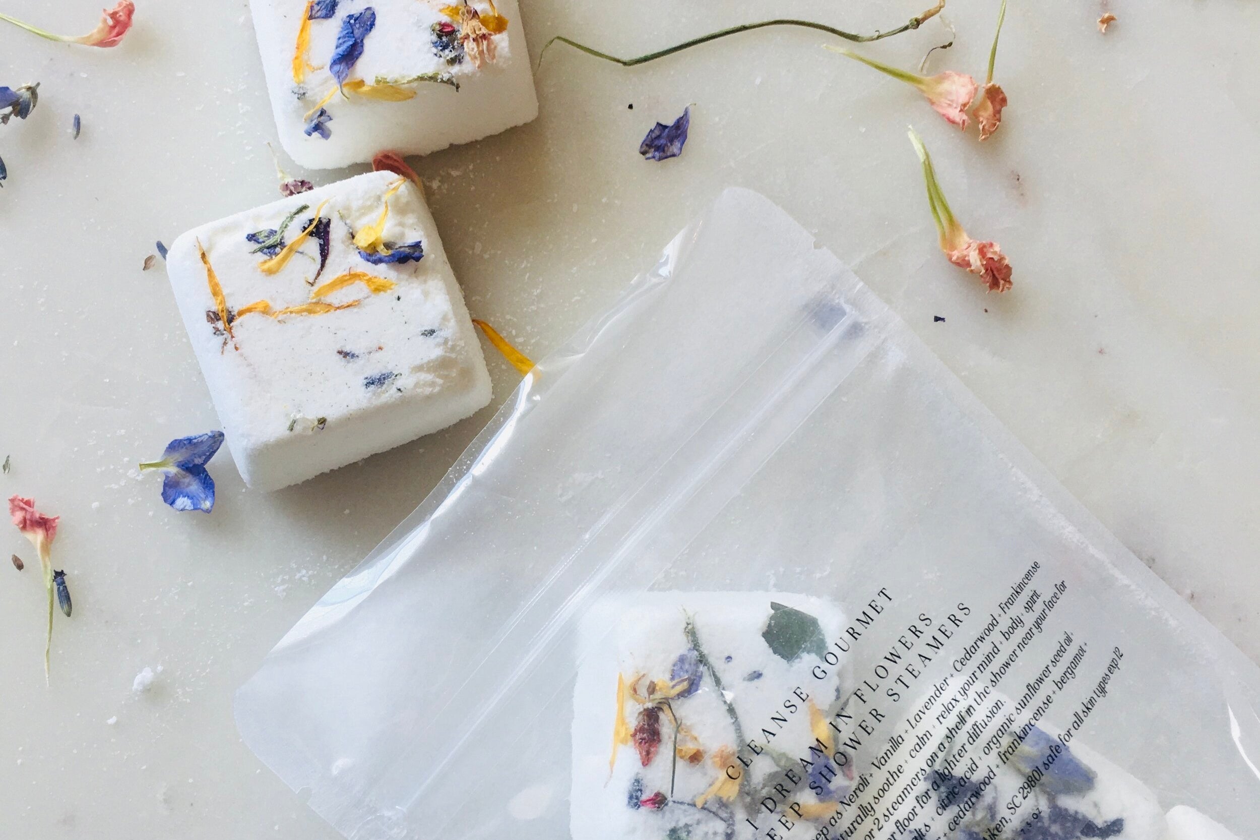 I Dream in Flowers Botanical Shower Steamers by Cleanse Gourmet with French lavender and vanilla essential oils. Five cubes in and out of packaging, surrounded by dried flowers. 