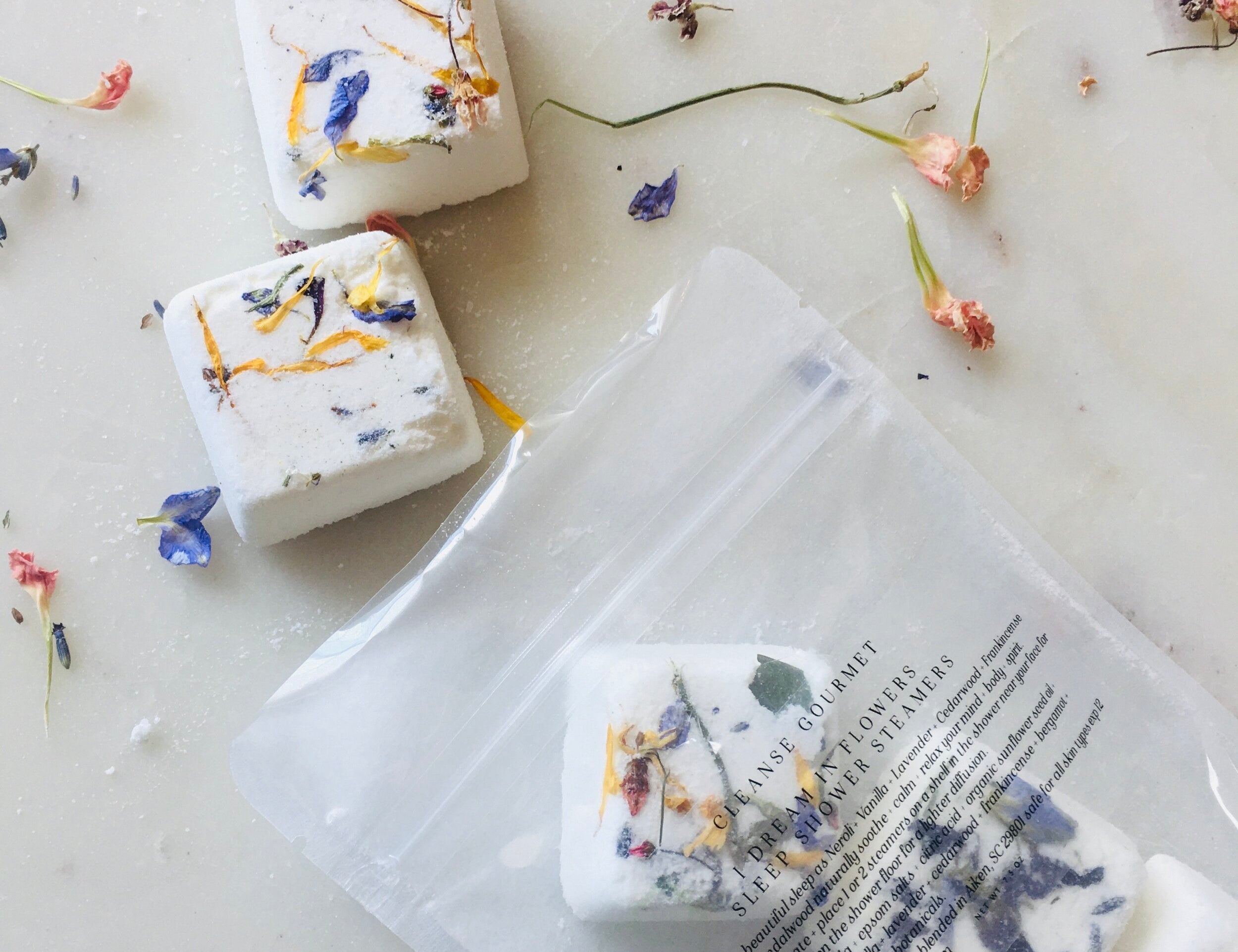 I Dream in Flowers Botanical Shower Steamers by Cleanse Gourmet with French lavender and vanilla essential oils. Five cubes in and out of packaging, surrounded by dried flowers. 