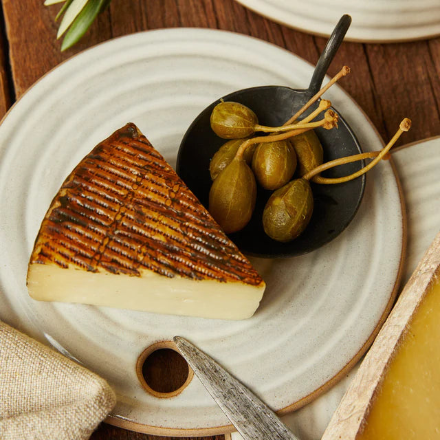 Handmade Forged Cast Iron Serving Dish with black matte finish and thin curving handle. Holding olives and next to cheese block on serving table.