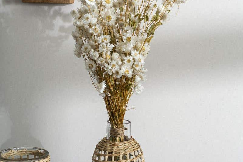 Two Jaxon Caraffes made of rattan covered glass, set in home and holding dried white flowers.