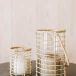 Two Glass Lieto Lanterns with rattan exterior and handle in natural light wood tone holding white candles and set in airy home