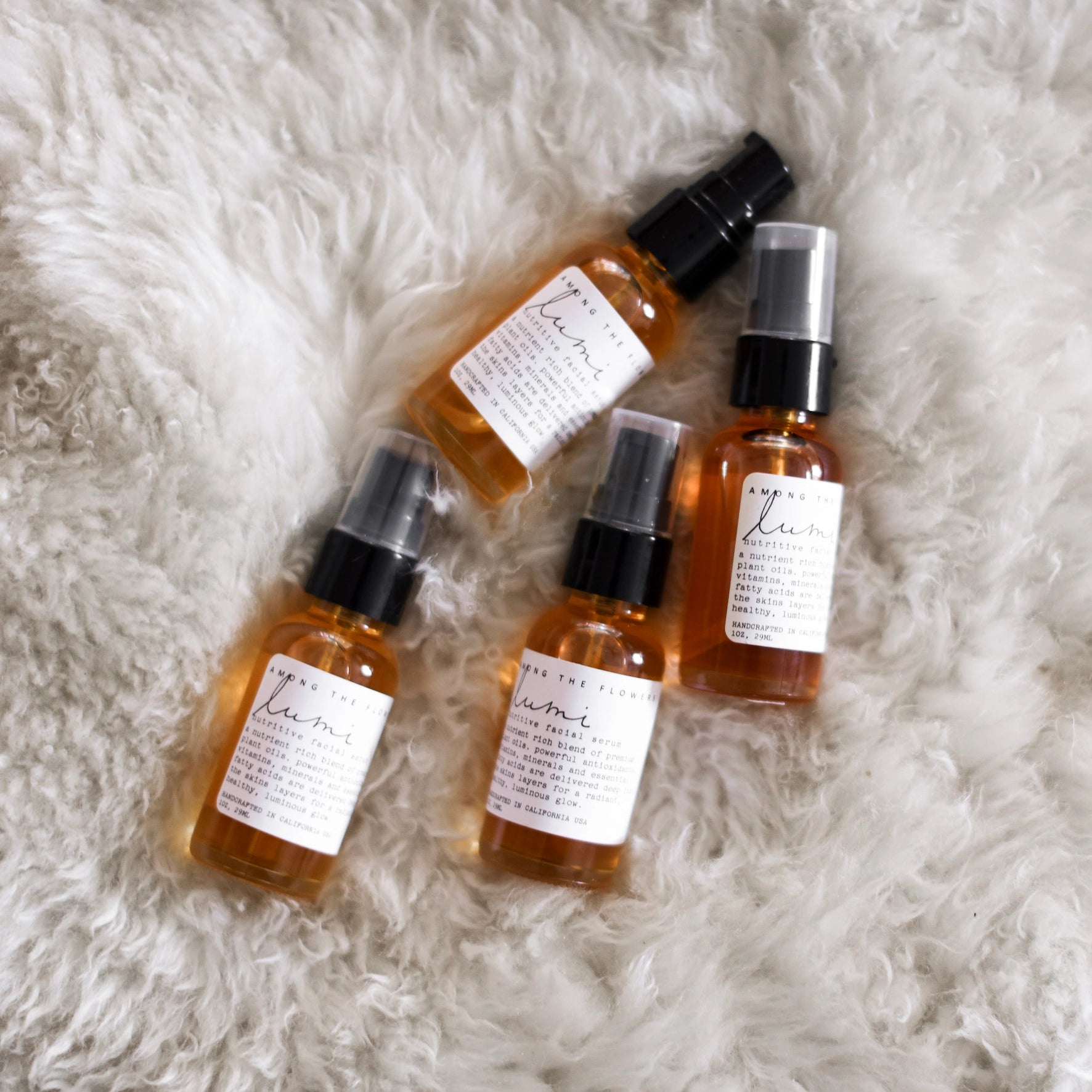 Four amber glass spray bottles with white labels and black spray tops arranged on a white faux fur surface. The labels show the brand name 'The Home Fix' and scent names including 'Lemon' and 'Orange'.