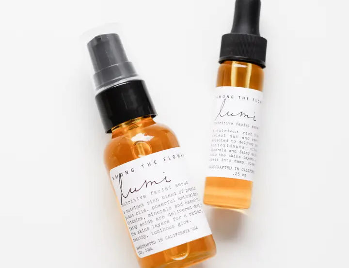 Two amber glass dropper and spray bottles with white labels, photographed on a clean white background. The label text appears to read 'Among the Flowers' and 'lumi'.