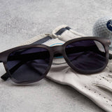 Black sunglasses on a golf glove with a golf ball in the background