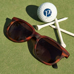 Sunglasses on a golf green with a golf ball and tees in the background