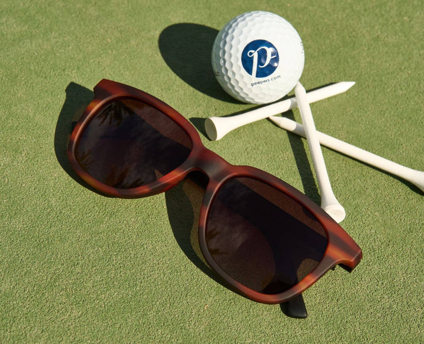 Sunglasses on a golf green with a golf ball and tees in the background