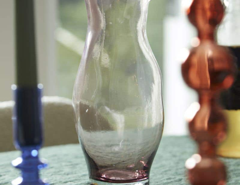 Minimal purple hued and mouth blown Onda Pitcher by Accent Decor on table between colorful candle holders. 