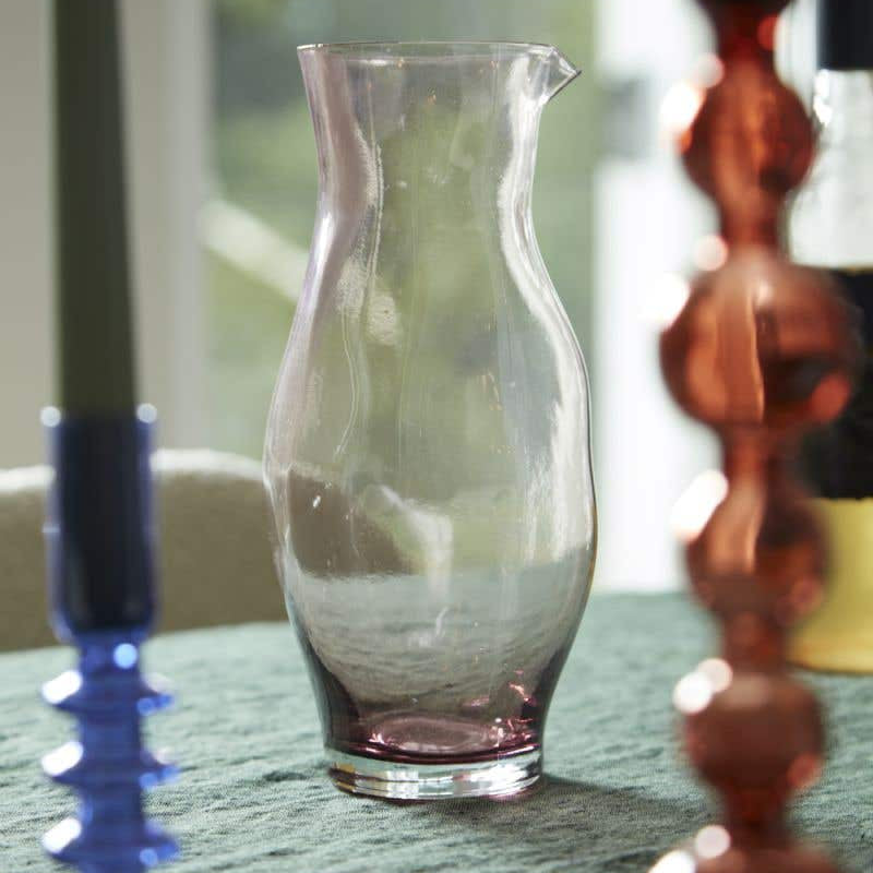 Minimal purple hued and mouth blown Onda Pitcher by Accent Decor on table between colorful candle holders. 