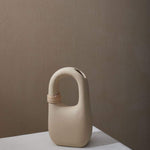 Palau Tan Vase matte finish with natural bisque cermaic, unique handle feature and wrapped rattan coil.  Sitting on stone table and backed by brown wall.