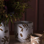 Three Rustling Pots collection pieces with oak leaves and acorns pattern in white glazed ceramic and natural bisque, set on dinner table.