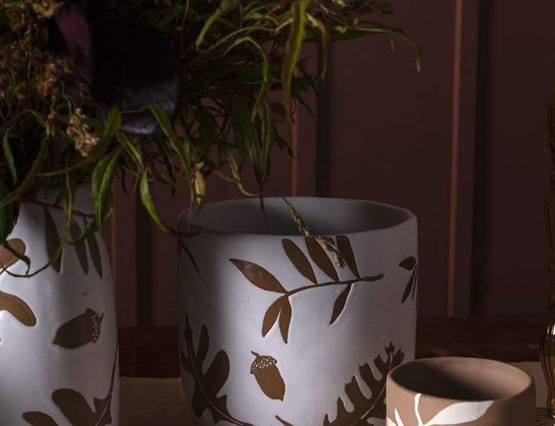 Three Rustling Pots collection pieces with oak leaves and acorns pattern in white glazed ceramic and natural bisque, set on dinner table.