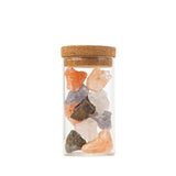 Clear glass jar with cork lid containing multicolored stones on a white background