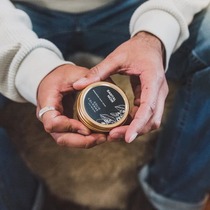 Man holding Santal Noir Solid Cologne in black and gold luxury tin