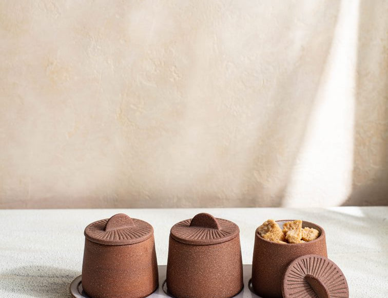 Canyon Decorative Spice Jars by Citrine Set of 3. Crafted from exposed reddish-brown earthenware with white glaze. Paired with tray and one lid off and holding sugar cubes.