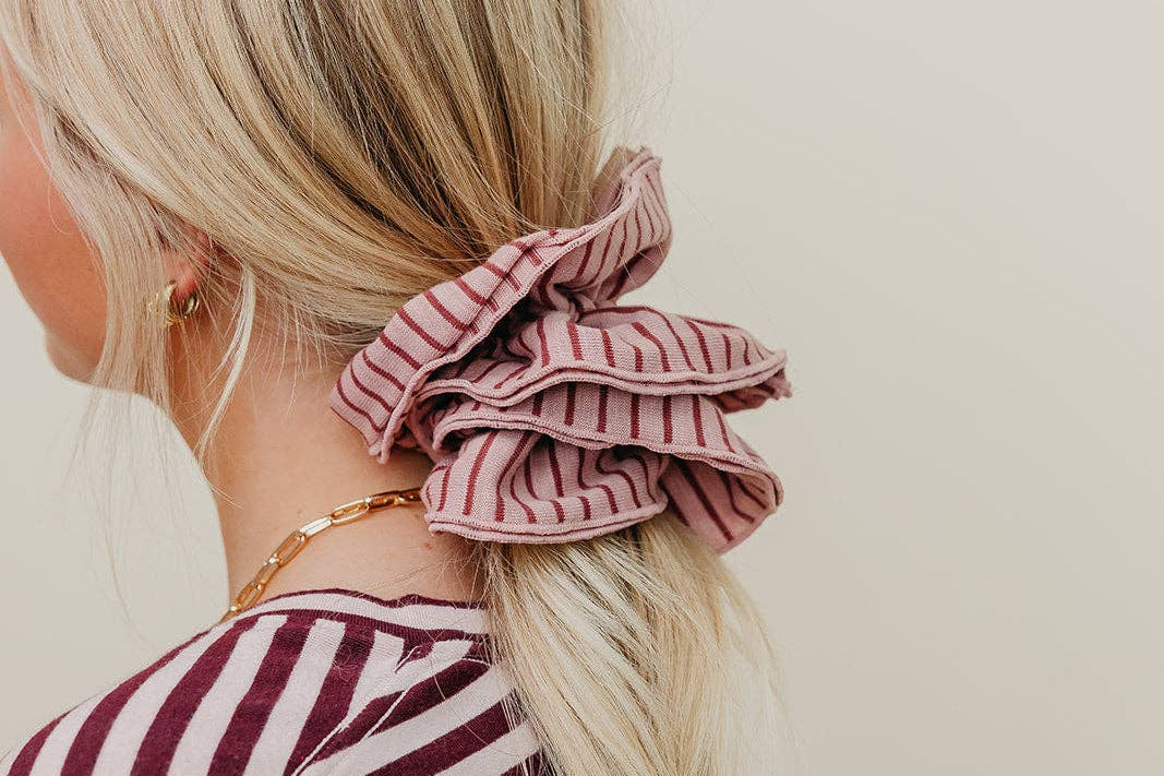 Person with a pink striped scrunchie in their hair against a plain background