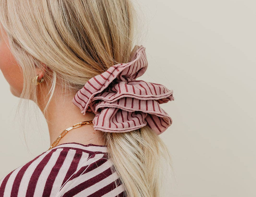 Person with a pink striped scrunchie in their hair against a plain background