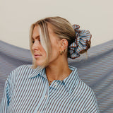 Woman wearing a striped shirt with a scrunchie on her head against a striped fabric background