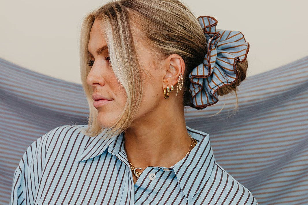 Woman wearing a striped shirt with a scrunchie on her head against a striped fabric background