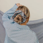 Person wearing a blue striped shirt with a scrunchie on their head against a neutral background