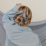Person wearing a blue striped shirt with a scrunchie on their head against a neutral background