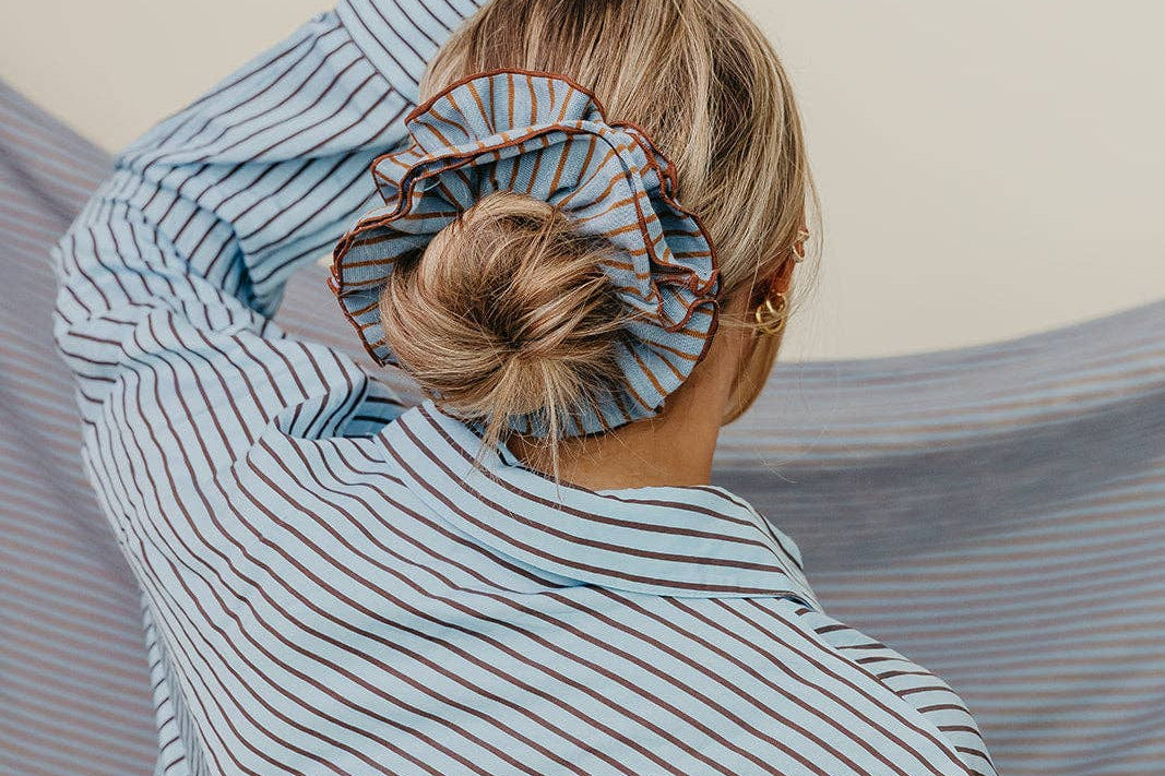 Person wearing a blue striped shirt with a scrunchie on their head against a neutral background