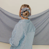 Person wearing a striped shirt with a blue scrunchie on their head, standing in front of a striped fabric backdrop.
