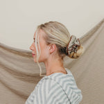 Woman with a bun and hair extensions standing against a beige curtain.