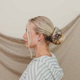 Woman with a bun and hair extensions standing against a beige curtain.