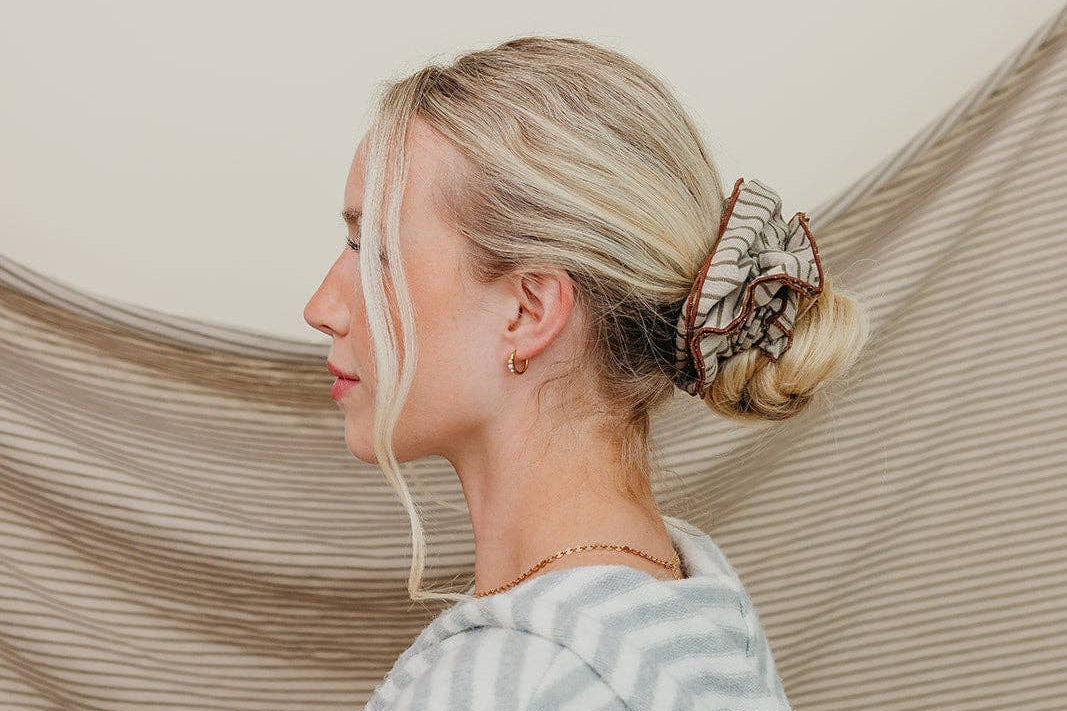 Woman with a bun and hair extensions standing against a beige curtain.
