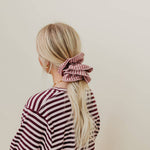 Person wearing a striped shirt with a pink scrunchie in their hair against a beige background