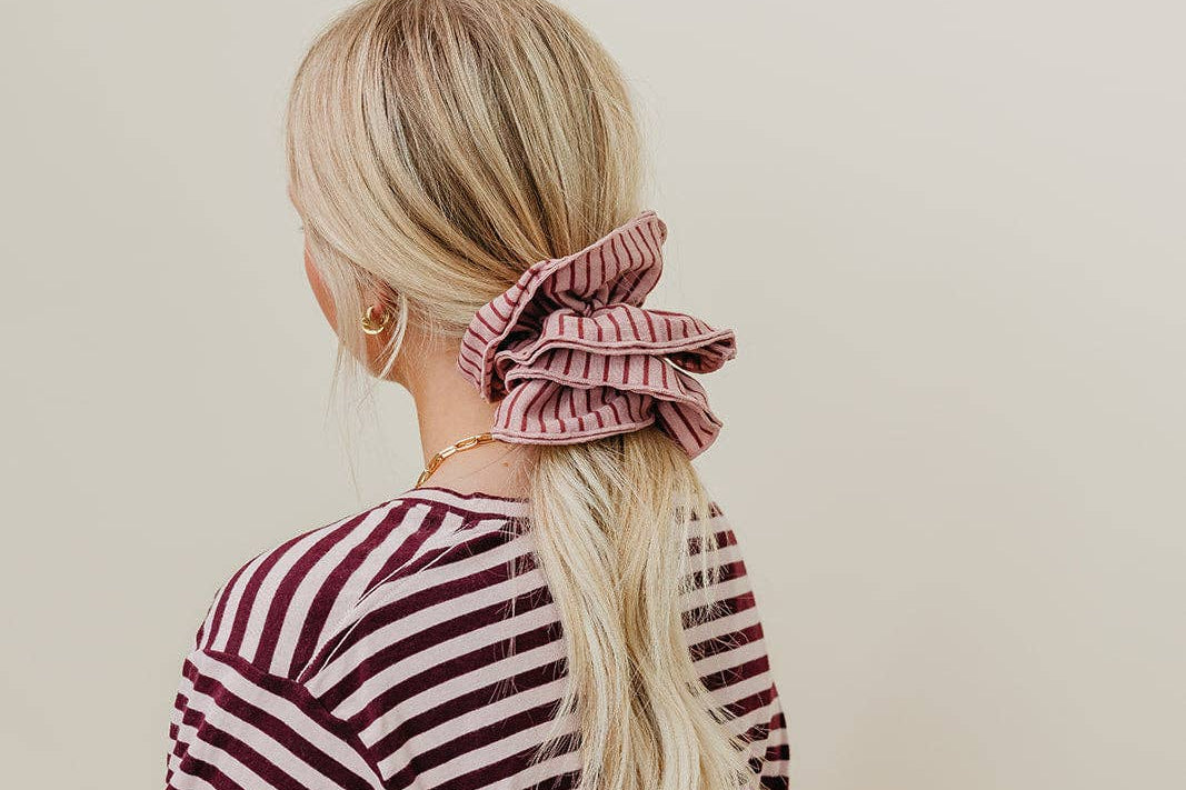 Person wearing a striped shirt with a pink scrunchie in their hair against a beige background