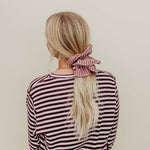 Person wearing a striped shirt with a pink scrunchie in their hair against a beige background
