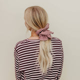 Person wearing a striped shirt with a pink scrunchie in their hair against a beige background