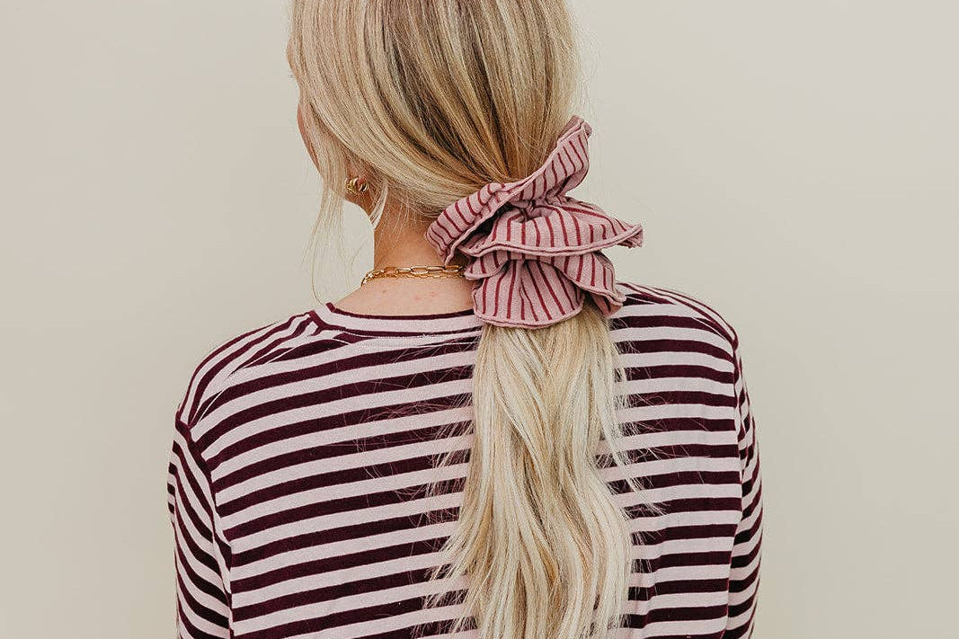 Person wearing a striped shirt with a pink scrunchie in their hair against a beige background