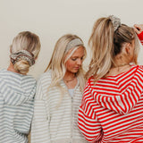 Three women with styled hair, wearing striped sweaters, against a plain background.