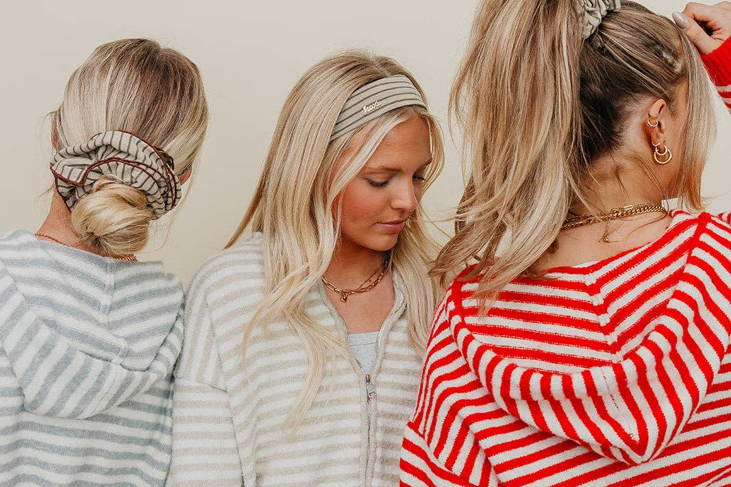 Three women with styled hair, wearing striped sweaters, against a plain background.