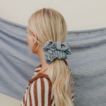 Person with a blue scrunchie in their hair against a striped fabric background