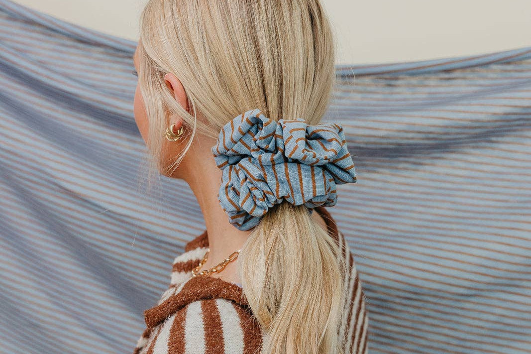 Person with a blue scrunchie in their hair against a striped fabric background