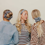 Three women wearing striped shirts and scrunchies with a neutral background