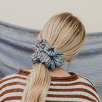 Person with a striped scrunchie in their hair, standing against a blurred natural background