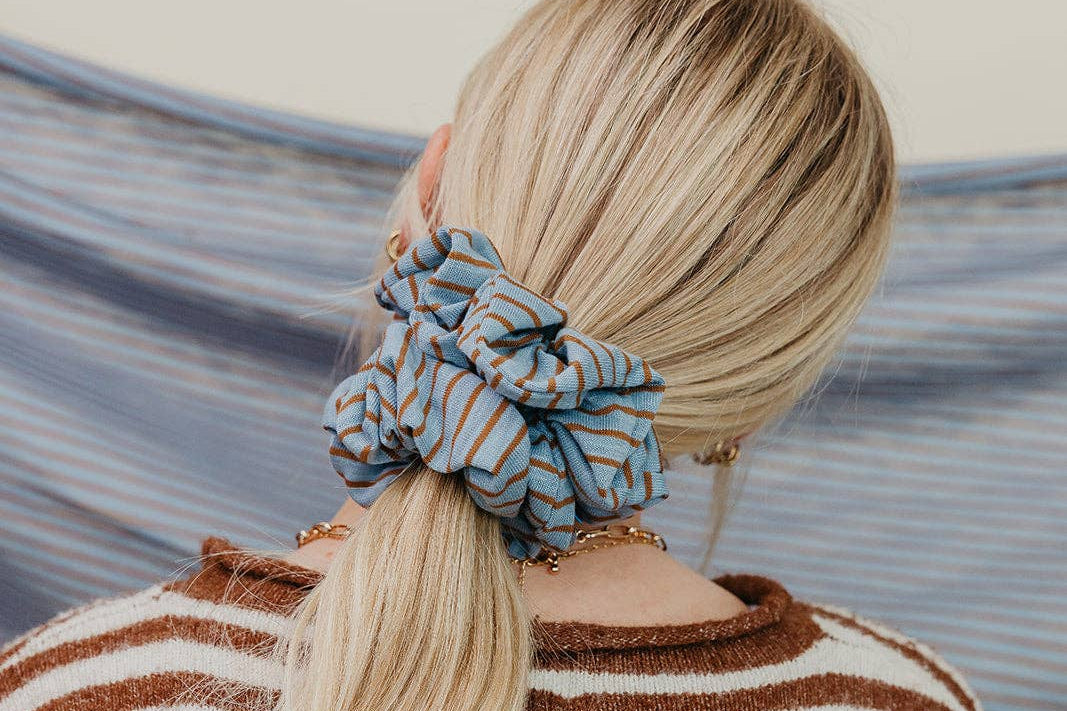 Person with a striped scrunchie in their hair, standing against a blurred natural background