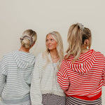 Three women wearing matching striped pajama sets against a plain background