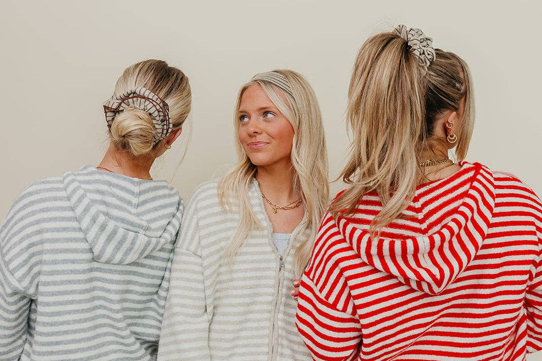 Three women wearing matching striped pajama sets against a plain background