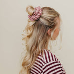 Woman with styled hair and a pink scrunchie against a neutral background